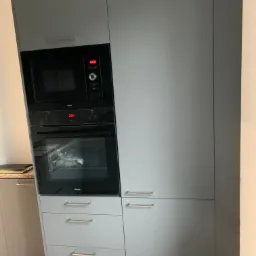 Szare szafki kuchenne z wbudowanym piekarnikiem i mikrofalówką marki Amica, widoczne srebrne uchwyty.