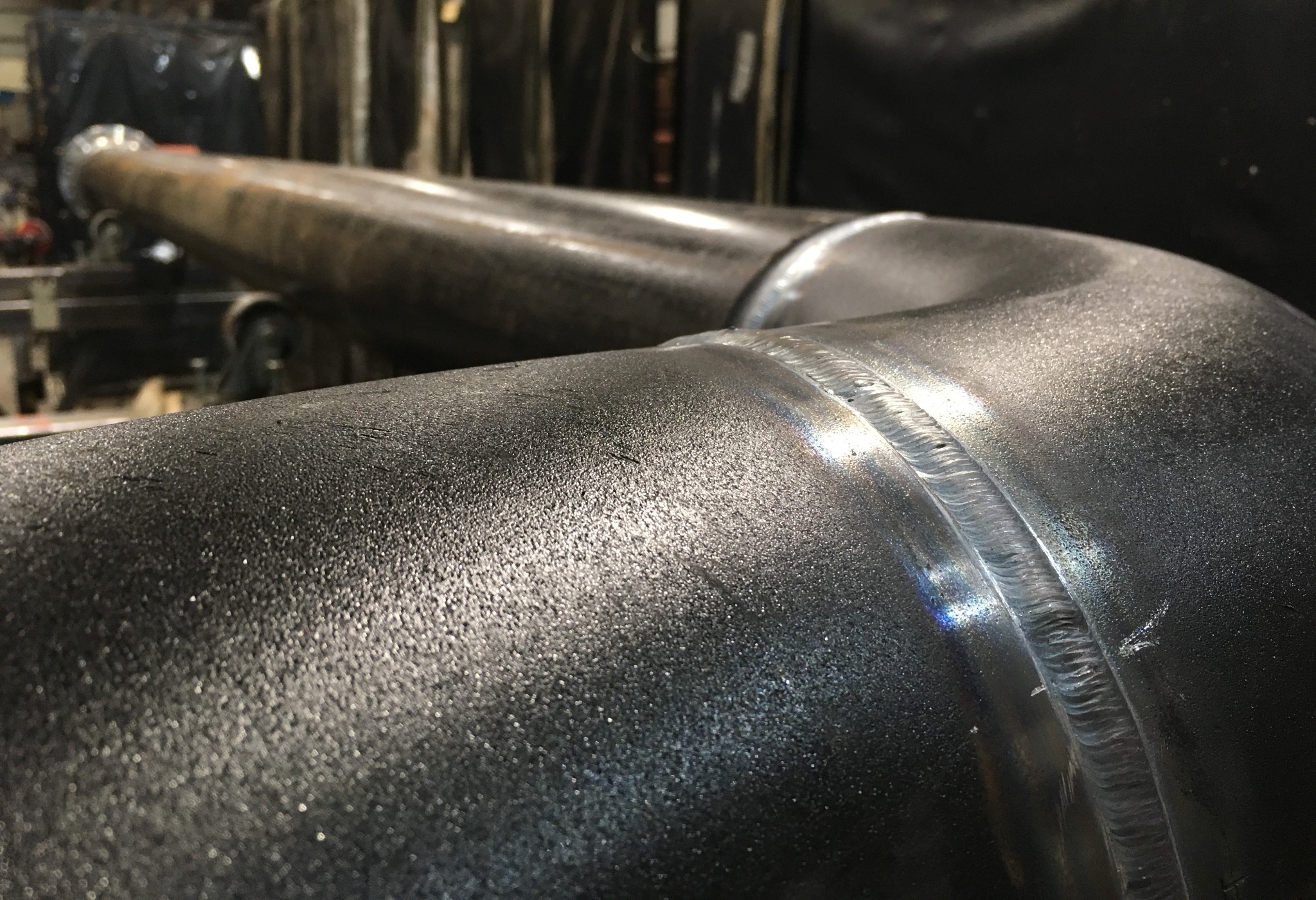 Spoina na grubościennej rurze z widoczną strukturą metalu i tęczowymi refleksami światła.