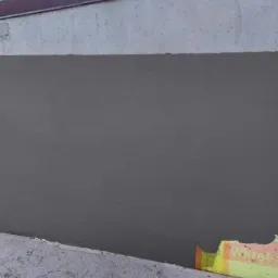 Świeżo nałożona, ciemnoszara warstwa wykończeniowa na ścianie zewnętrznej budynku, widoczny fragment ocieplenia przy podłożu.