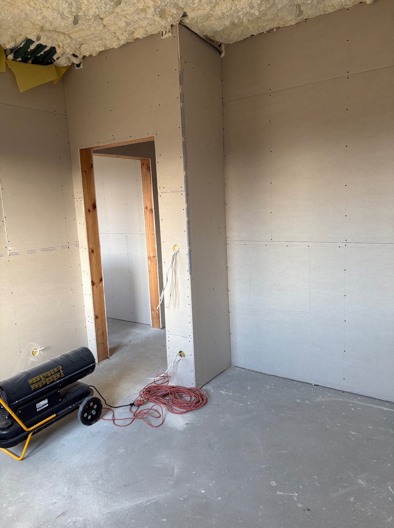 Wnętrze w trakcie budowy domu szkieletowego: ściany z płyt gipsowo-kartonowych, izolacja piankowa na suficie, nagrzewnica i kable na podłodze, widoczne drewniane elementy konstrukcyjne.