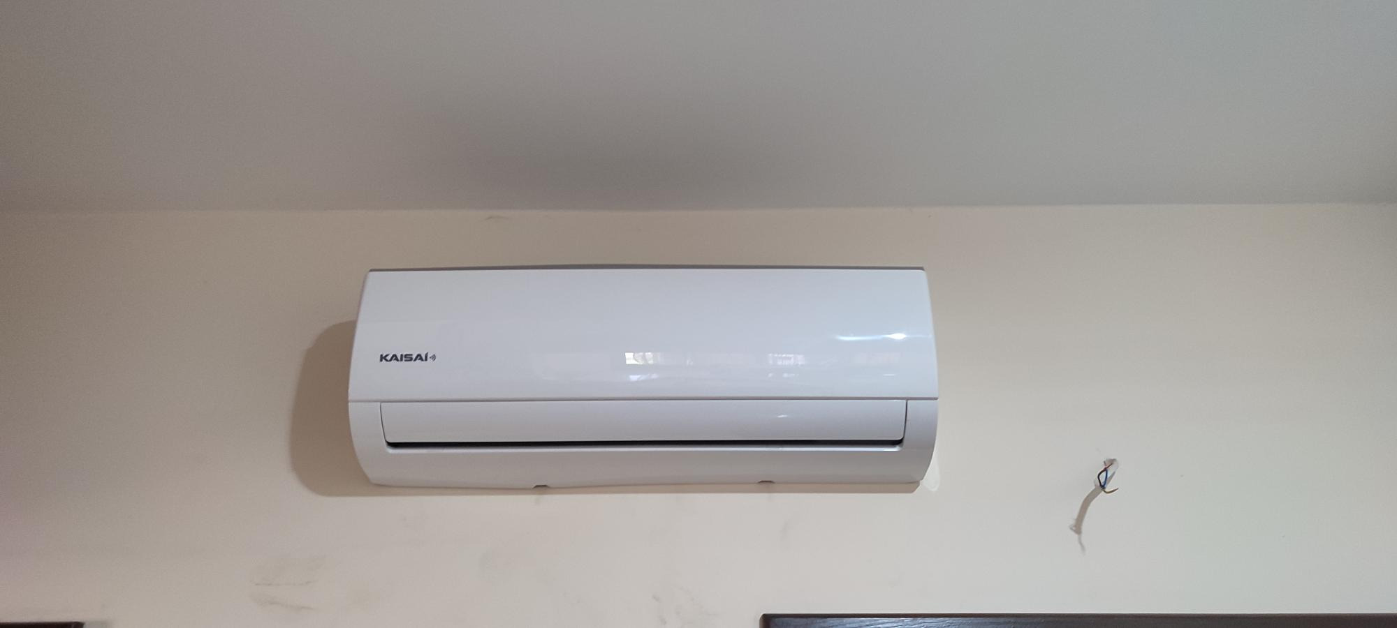Biały klimatyzator marki Kaisai zamontowany na jasnej ścianie z widocznymi przewodami po instalacji.