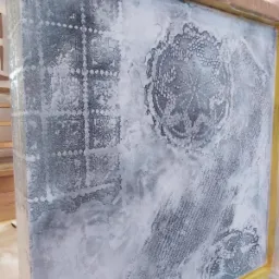 Dekoracyjna ściana z efektem przetarć i wzorami imitującymi koronki, zabezpieczona folią malarską i taśmą, w trakcie malowania.