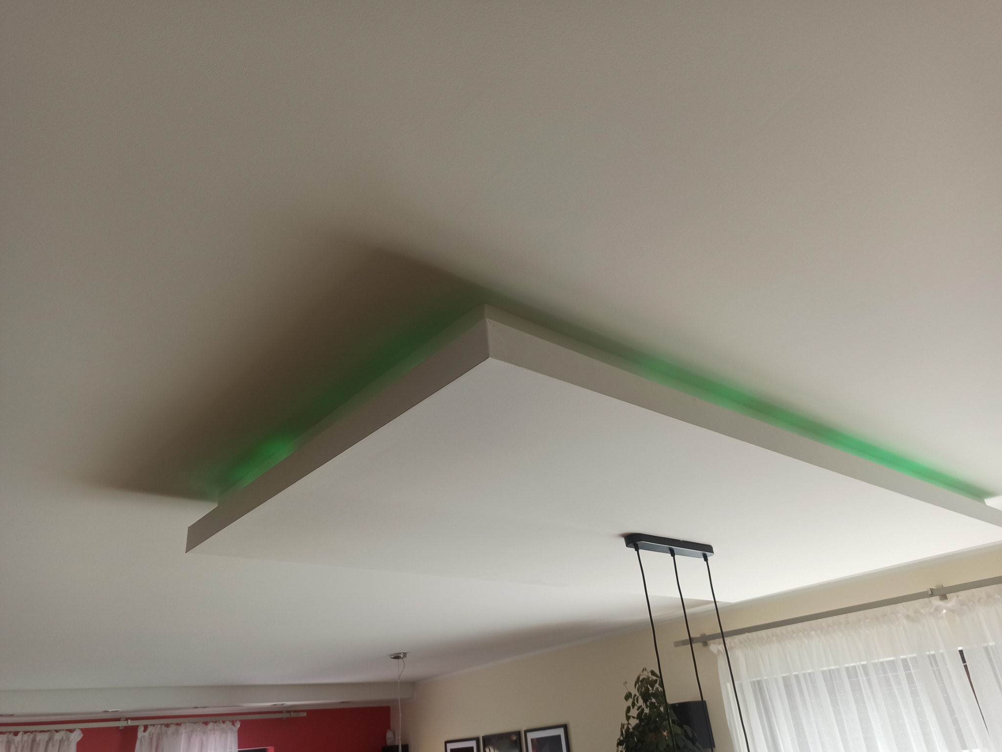 Biały sufit podwieszany z zielonym oświetleniem LED i wiszącą lampą na trzech przewodach w nowoczesnym salonie.