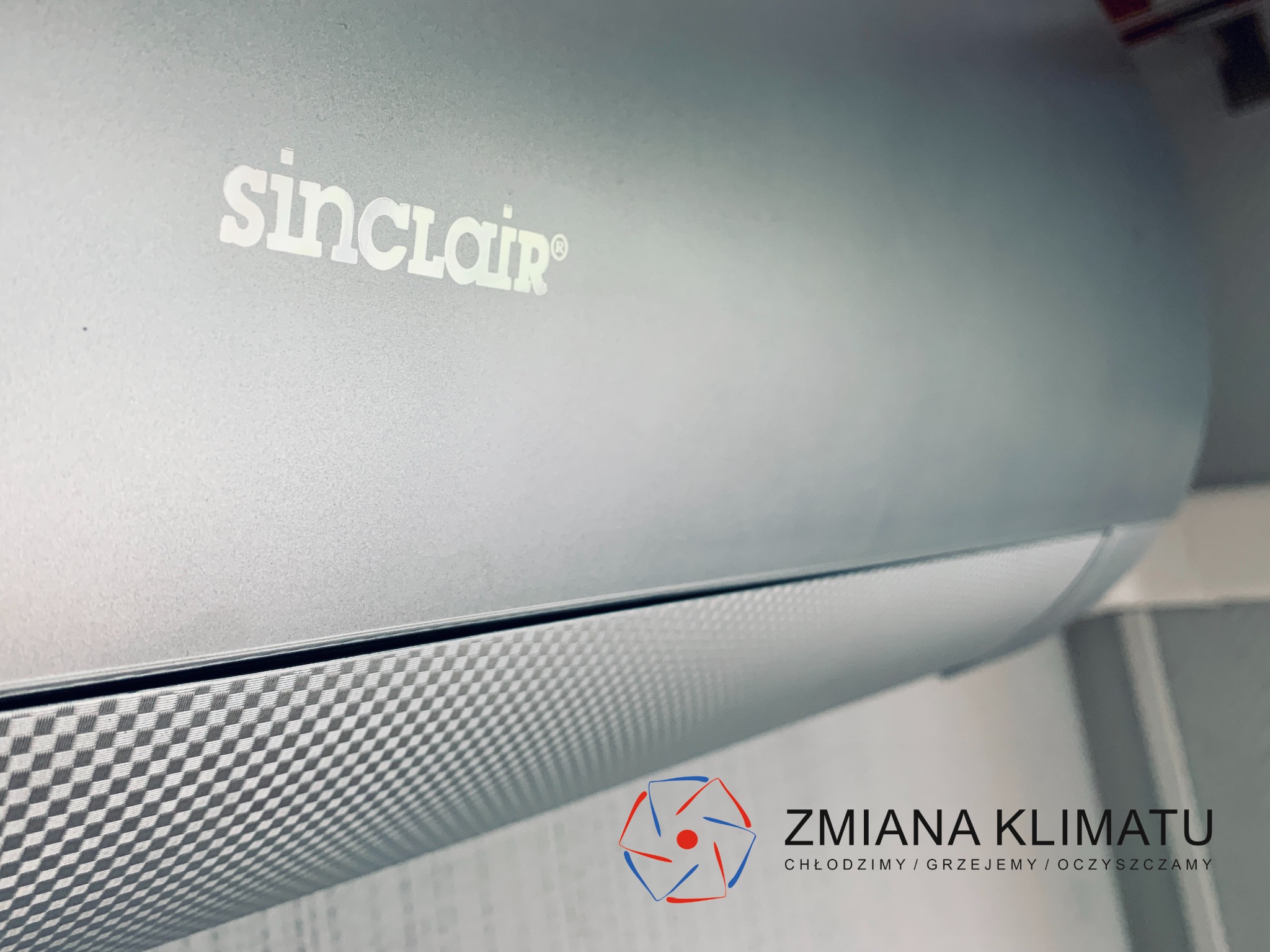 Szary klimatyzator Sinclair z widocznym logo firmy Zmiana Klimatu, zamontowany w pomieszczeniu.