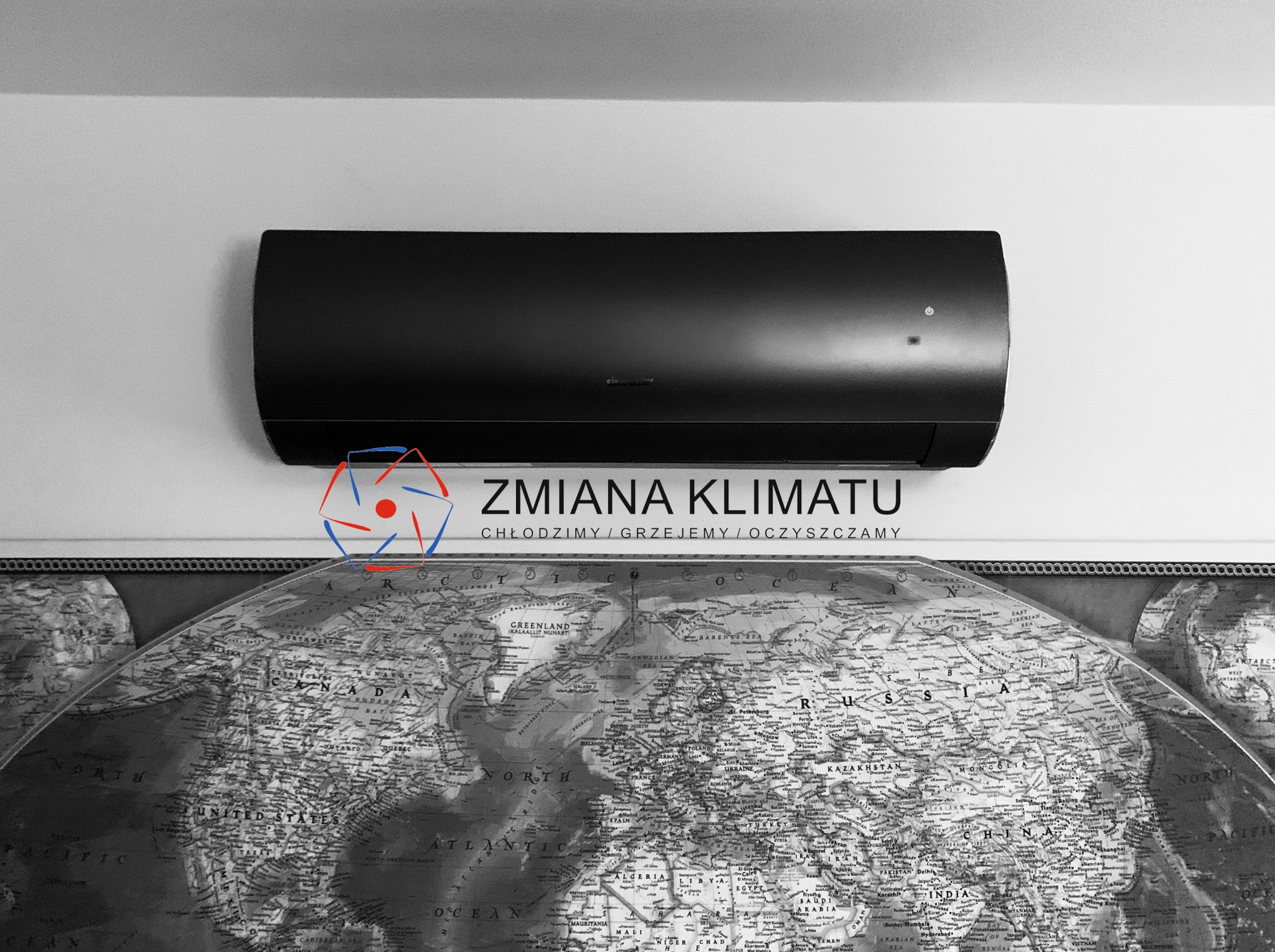 Czarny klimatyzator ścienny zamontowany nad dużą mapą świata, z widocznym logo firmy 'Zmiana Klimatu'.