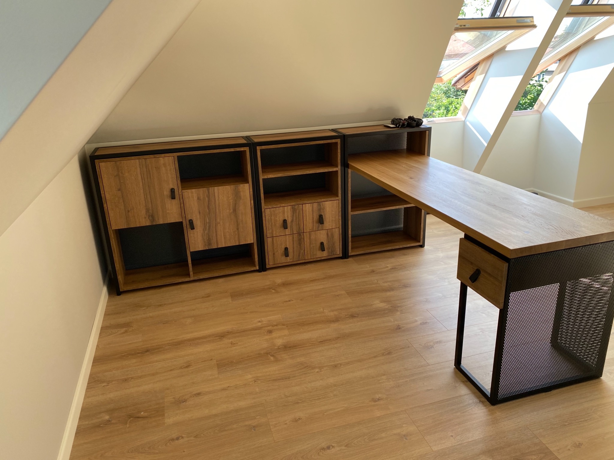 Zestaw mebli w stylu loftowym z drewnianymi frontami i metalowymi ramami, wkomponowany w przestrzeń pod skosami poddasza, z widocznymi oknami dachowymi i drewnianą podłogą.