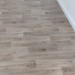 Ułożone panele podłogowe w jasnym odcieniu drewna, widoczna poziomica i nożyczki oraz maszyna do docinania paneli, przy białej ścianie z listwą przypodłogową.