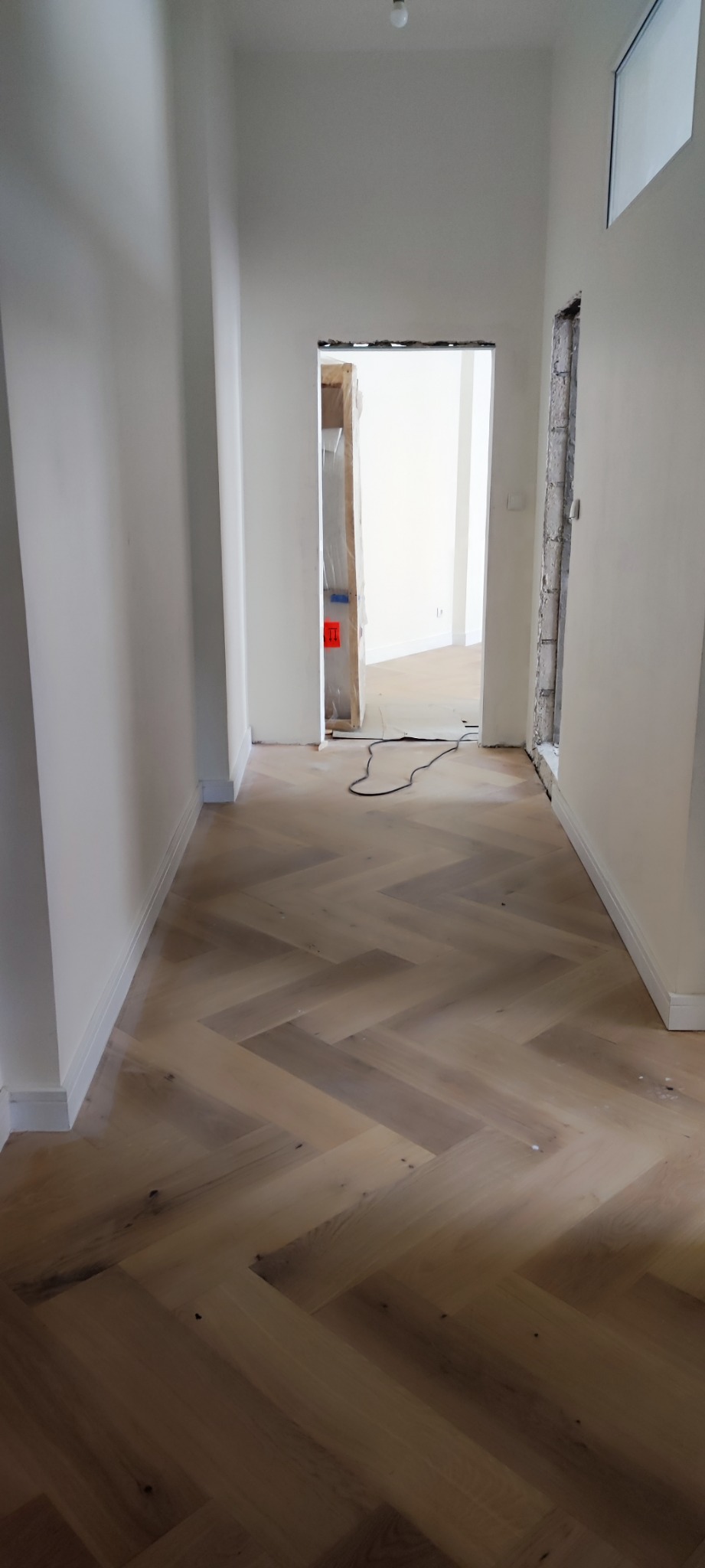 Ułożona podłoga z paneli w jodełkę w korytarzu, widoczne przygotowania do montażu ościeżnicy drzwiowej.