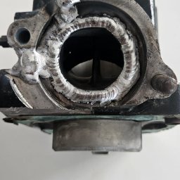 Spawmex Michał Ożóg - Szczegółowe zbliżenie na spoinę aluminium wokół otworu w metalowym elemencie, ukazujące naprawę spawalniczą z wyraźnymi śladami spawania.