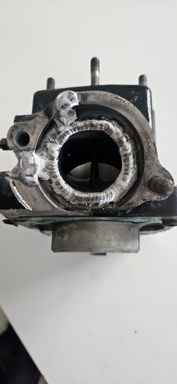 Szczegółowe zbliżenie na spoinę aluminium wokół otworu w metalowym elemencie, ukazujące naprawę spawalniczą z wyraźnymi śladami spawania.