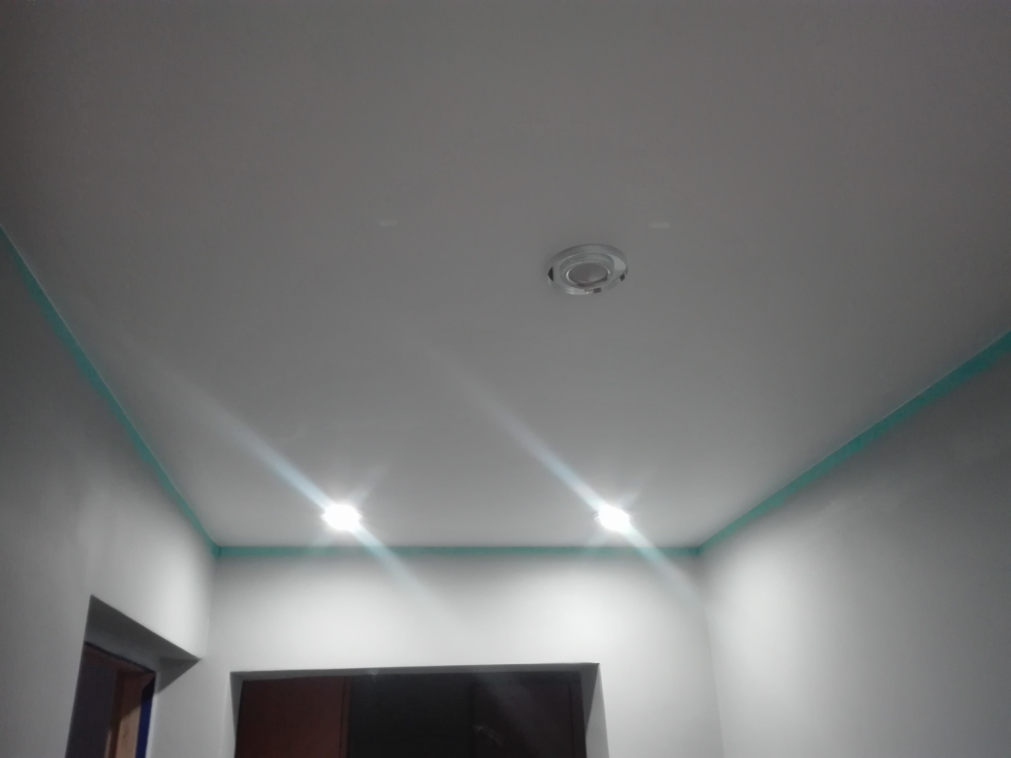 Świeżo pomalowany sufit i ściany na biało z dekoracyjną, turkusową listwą przy suficie, widoczne dwa punkty oświetleniowe i fragmenty dwóch otworów drzwiowych.
