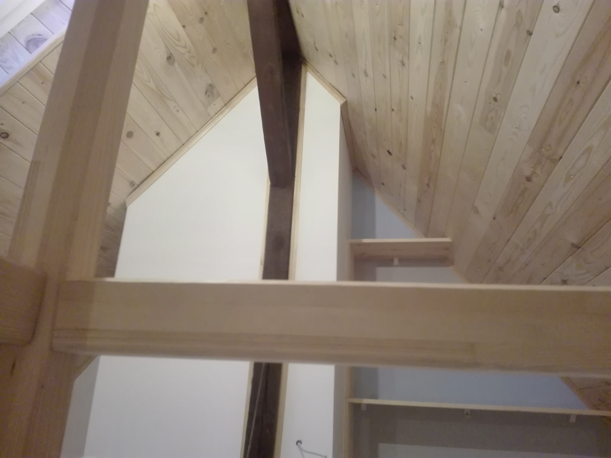 Drewniana konstrukcja stropu i schodów w trakcie budowy, widoczne deski na suficie i elementy nośne, jasne drewno, surowy stan.