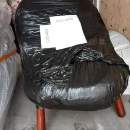 Krzesło owinięte czarną folią stretch z naklejoną kartką z numerem CVO-4628, przygotowane do transportu wewnątrz pojazdu.