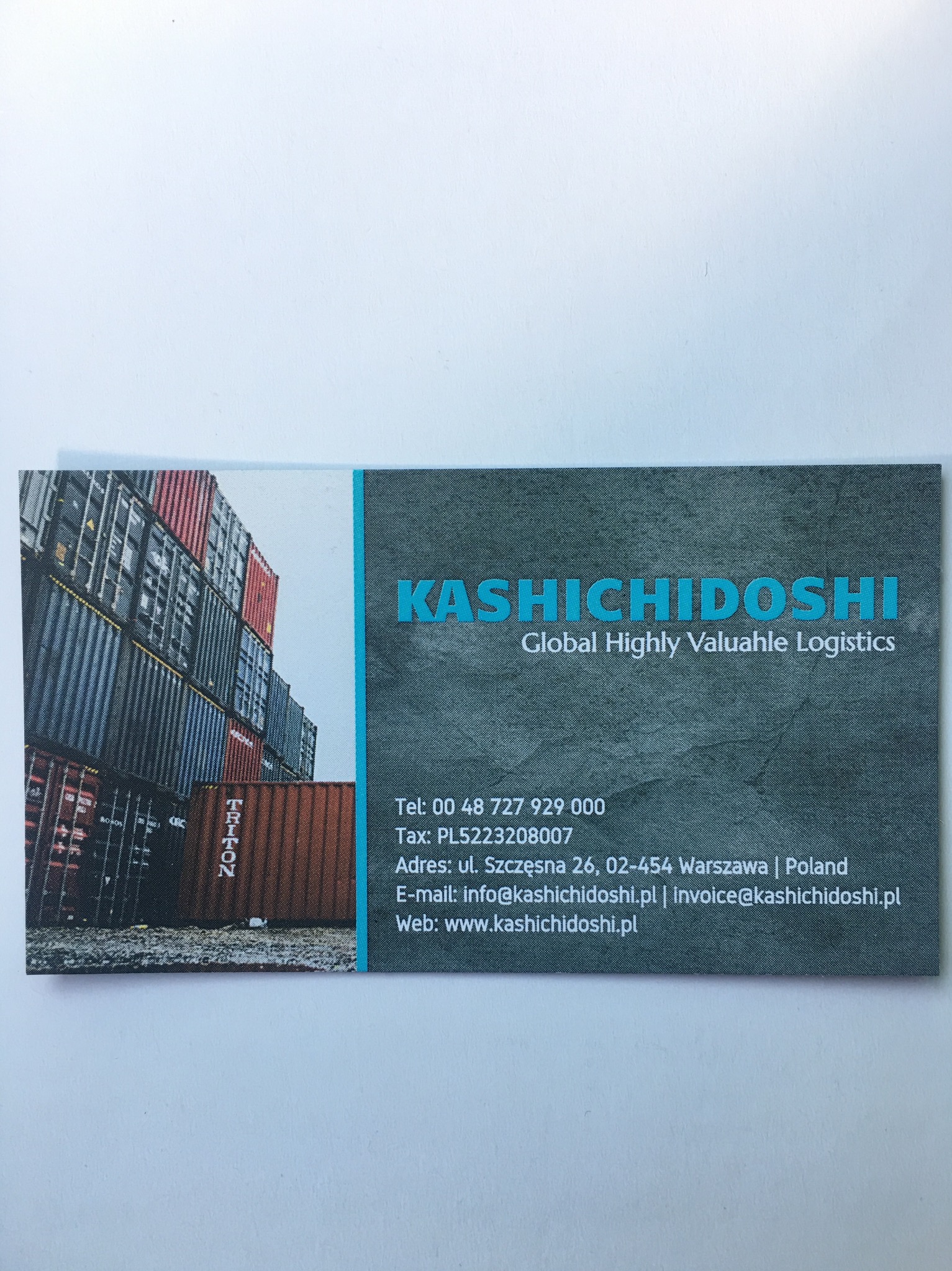 Wizytówka firmy logistycznej Kashichidoshi z ilustracją kontenerów transportowych w porcie.