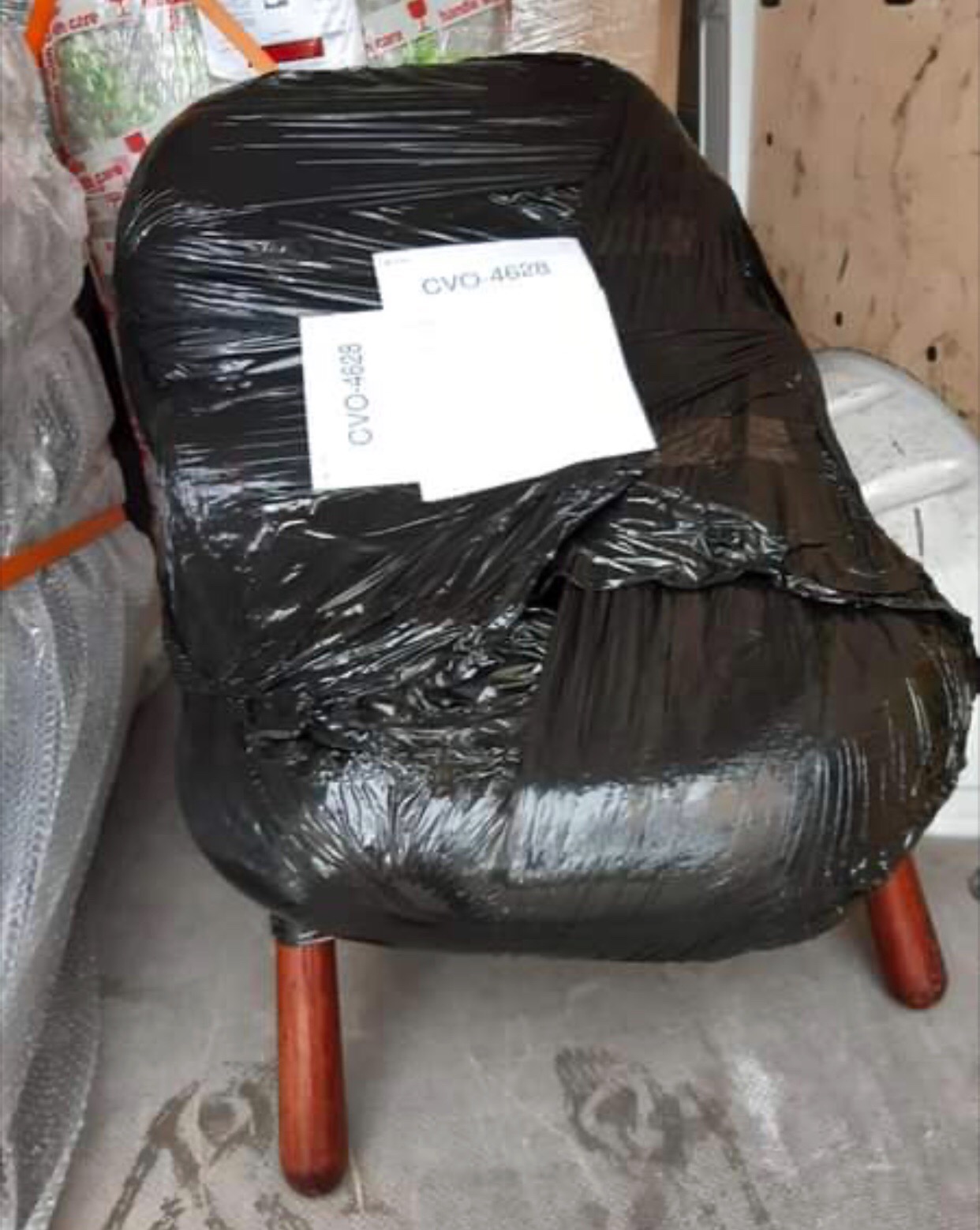Krzesło owinięte czarną folią stretch z naklejoną kartką z numerem CVO-4628, przygotowane do transportu wewnątrz pojazdu.