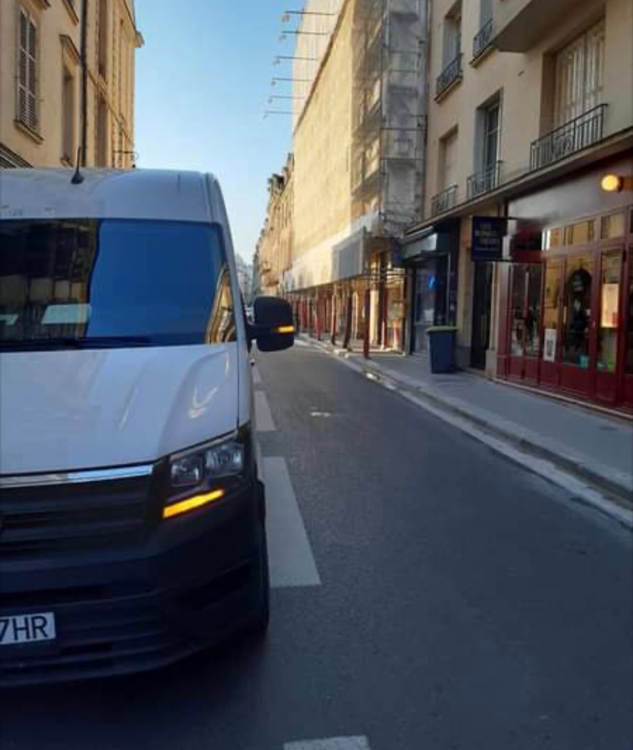 Biały bus transportowy zaparkowany na wąskiej ulicy w europejskim mieście, widok z perspektywy ulicy.
