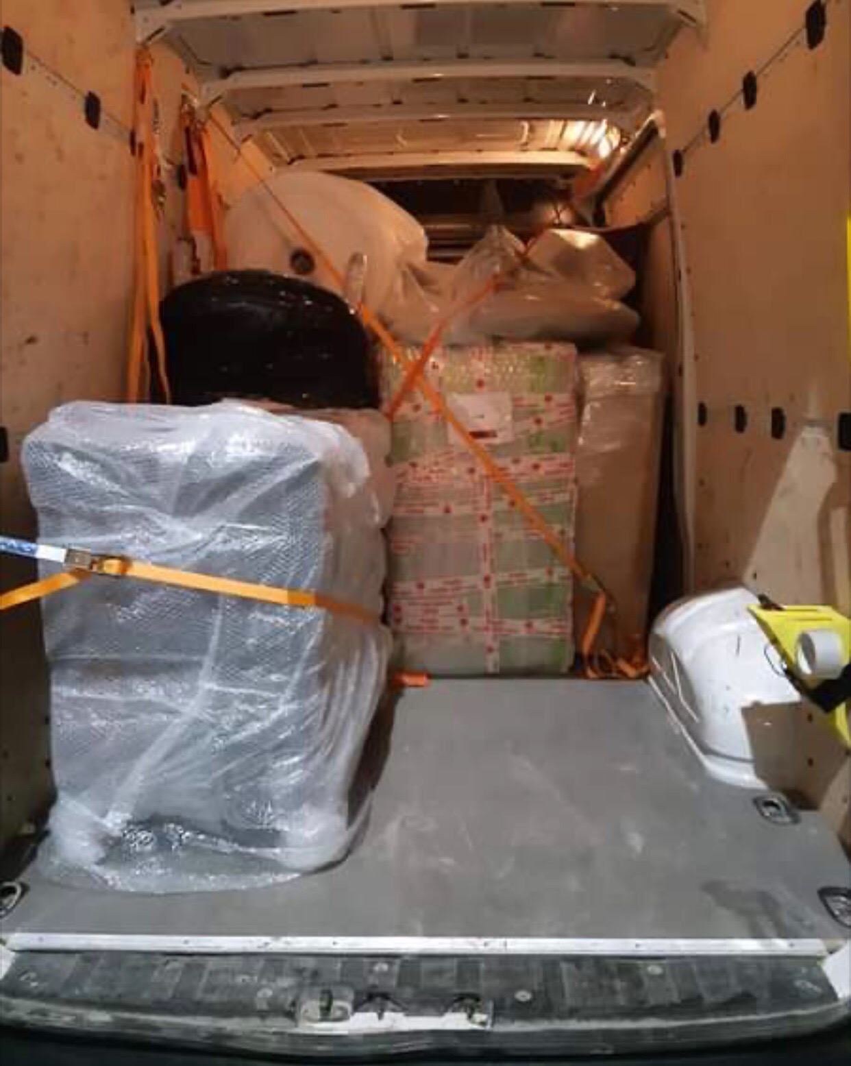 Wnętrze busa załadowane meblami i sprzętami zabezpieczonymi folią i pasami transportowymi, widok z tyłu pojazdu.