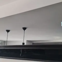 Nowoczesny, szary klimatyzator LG z wyświetlaczem temperatury (18 stopni) zamontowany na białej ścianie, z odbiciem lamp wiszących w obudowie.