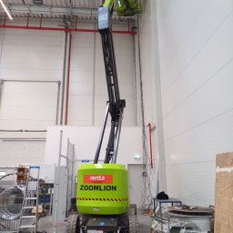 MEDIA M PATRYK KOWALCZUK - Wysięgnik koszowy z operatorem w hali produkcyjnej podczas montażu instalacji pod sufitem, widoczne kable i rury.