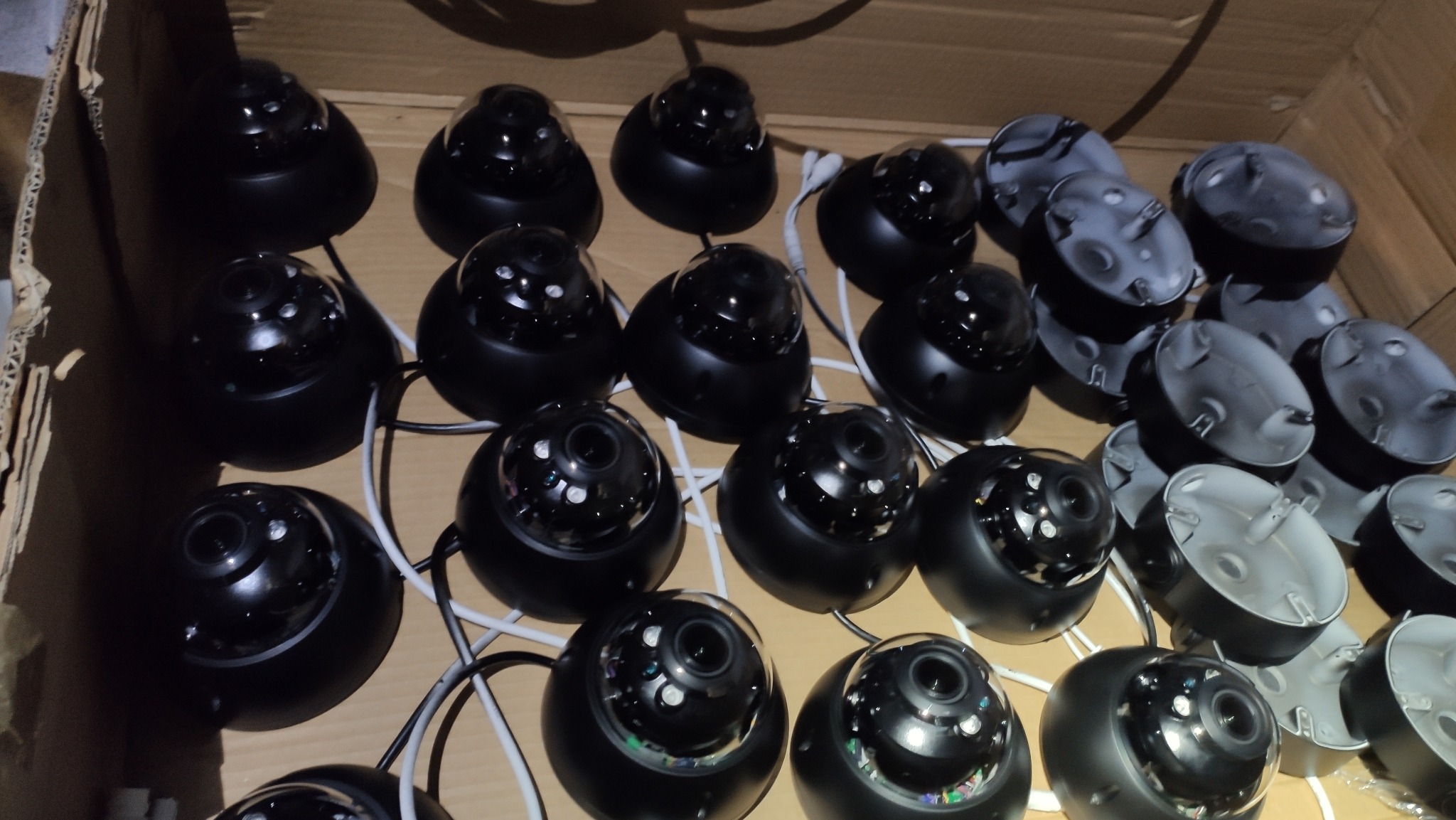 Partia czarnych kamer kopułkowych CCTV z widocznymi przewodami i uchwytami montażowymi w kartonowym pudełku.