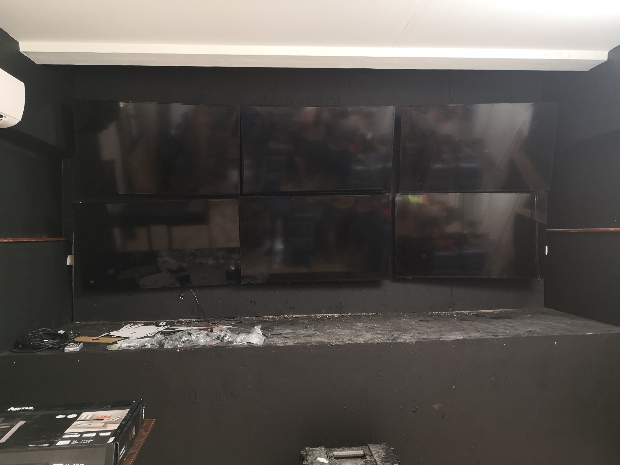 Sześć ekranów monitoringu zamontowanych na czarnej ścianie, widoczne kable, akcesoria montażowe i narzędzia na półce poniżej.