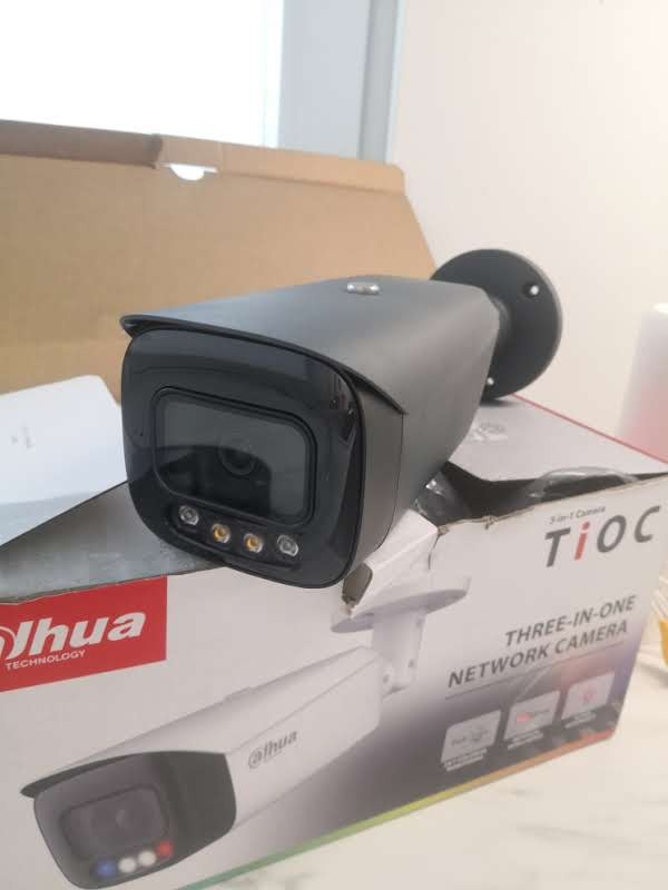 Czarna kamera sieciowa Dahua TiOC, leżąca na pudełku z jej wizerunkiem, widoczne diody LED i uchwyt montażowy.