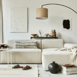 Jasny salon z modułową sofą, stolikiem pomocniczym z drewnianą misą, dywanem w stylu boho, lampą łukową i dekoracjami ściennymi w neutralnych barwach.