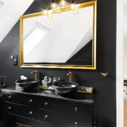 Elegancka łazienka na poddaszu w stylu glamour z czarnymi ścianami, dwiema czarnymi umywalkami na czarnej komodzie z szufladami, złotą armaturą, dużym lustrem w złotej ramie i oświetleniem punktowym.
