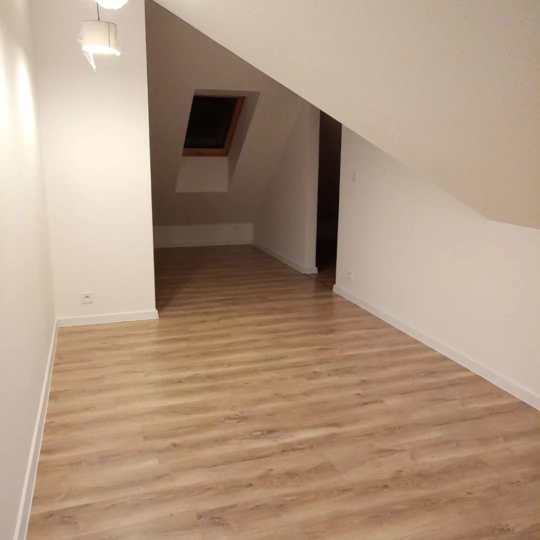 Poddasze po remoncie z nową podłogą laminowaną imitującą drewno, widoczne okno dachowe i świeżo pomalowane ściany na biało, lampa wisząca z papierowym abażurem w rogu.