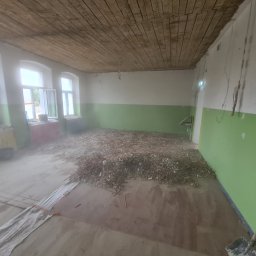 Od Nowa - Pokój w trakcie remontu: drewniany sufit, ściany z zielonym pasem, gruz na podłodze, szpachla i wiadro przy oknie, łopata oparta o ścianę.