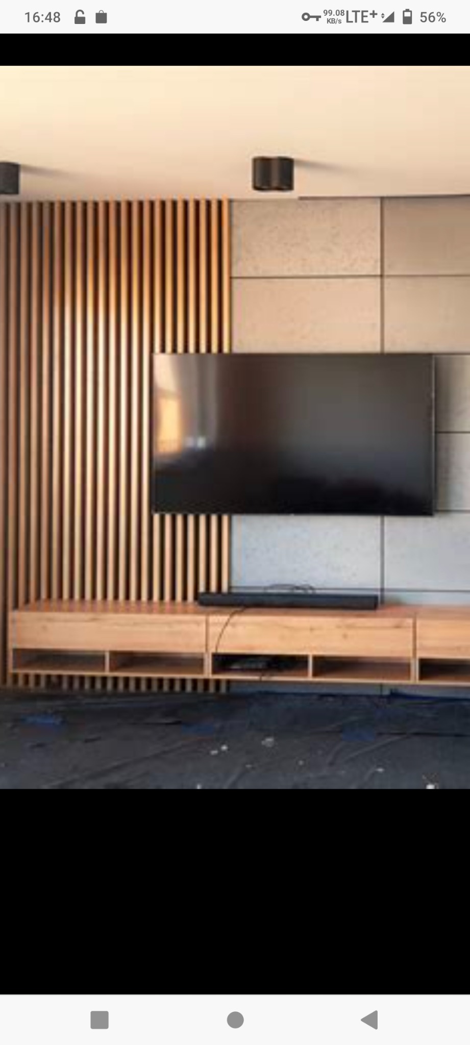 Nowoczesne wnętrze salonu z drewnianą ścianką działową z pionowych listew, panele ścienne imitujące beton, wiszący telewizor i szafka RTV z jasnego drewna.