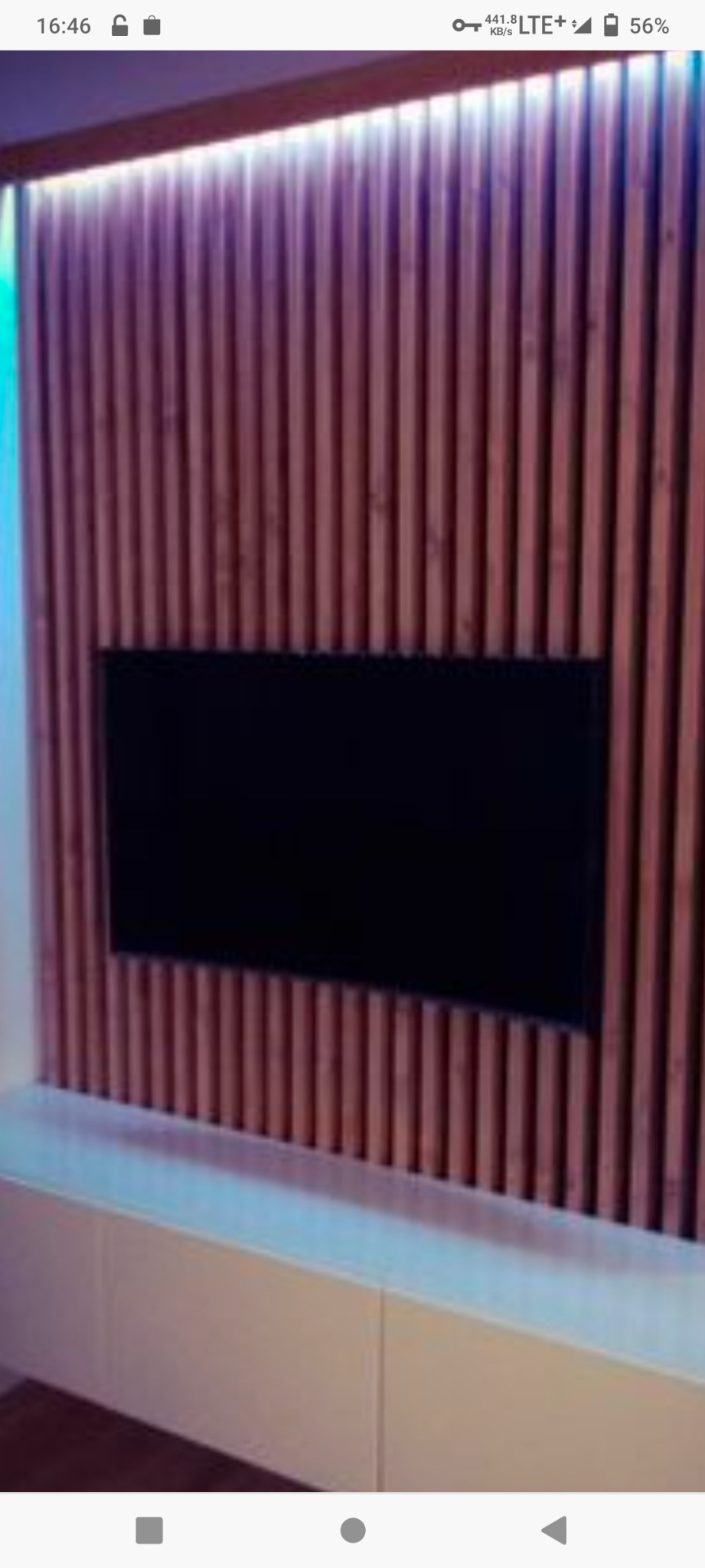 Ściana z drewnianych listew w kolorze jasnego drewna, z podświetleniem LED u góry i zamontowanym telewizorem, na dole biała zabudowa