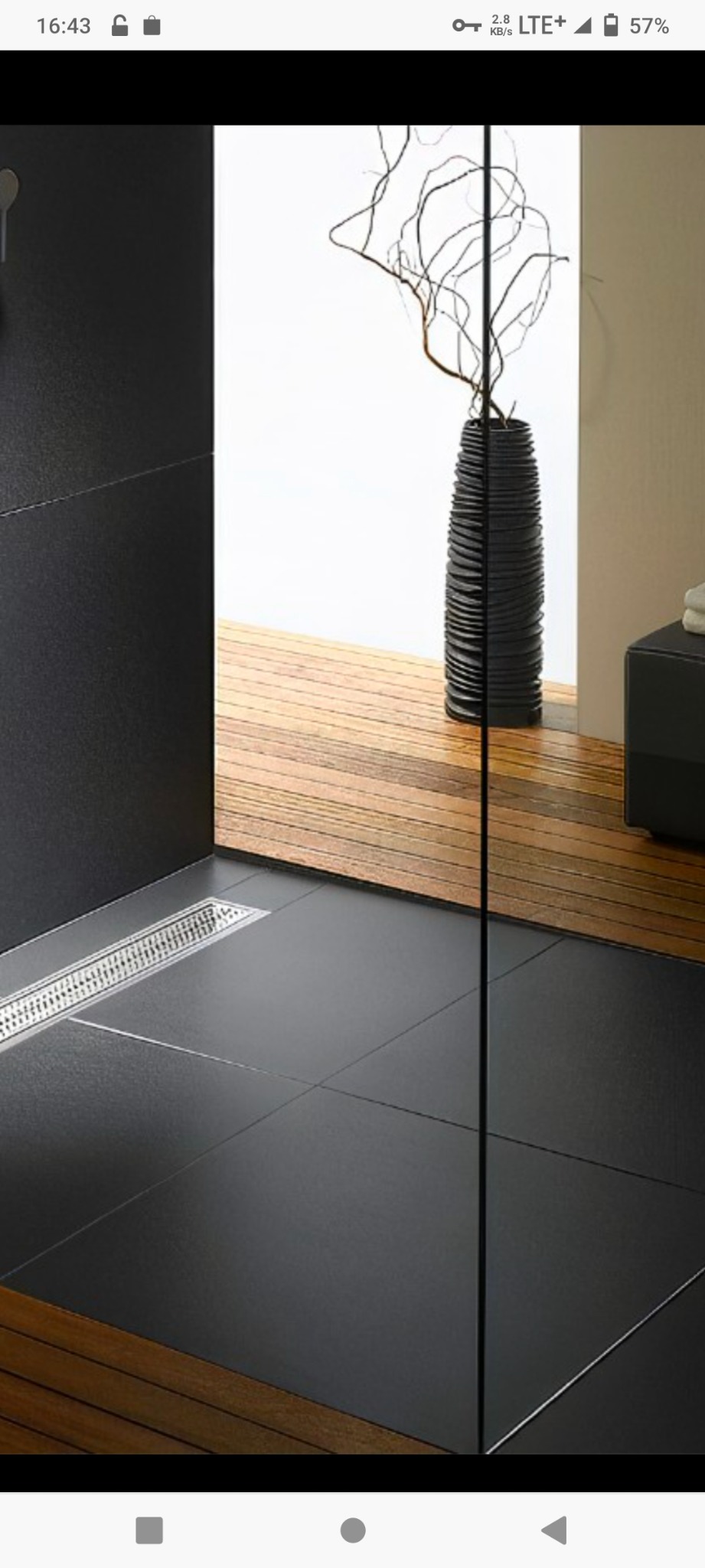 Nowoczesna łazienka z czarnymi płytkami podłogowymi, drewnianym wykończeniem pod prysznicem typu walk-in i ozdobnym wazonem z gałęziami w tle.