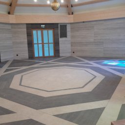uslugi remontowo budowlane - Wnętrze kościoła z geometrycznym wzorem na podłodze z płytek, jasne ściany z efektem marmuru, drewniane belki stropowe i rzeźba ukrzyżowanego Chrystusa po prawej.