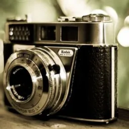 Vintage aparat Kodak Retinette 1B z obiektywem Rodenstock, Prontor 500 LK na drewnianej powierzchni, z rozmytym zielonym tłem.