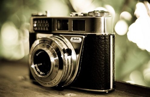 Vintage aparat Kodak Retinette 1B z obiektywem Rodenstock, Prontor 500 LK na drewnianej powierzchni, z rozmytym zielonym tłem.