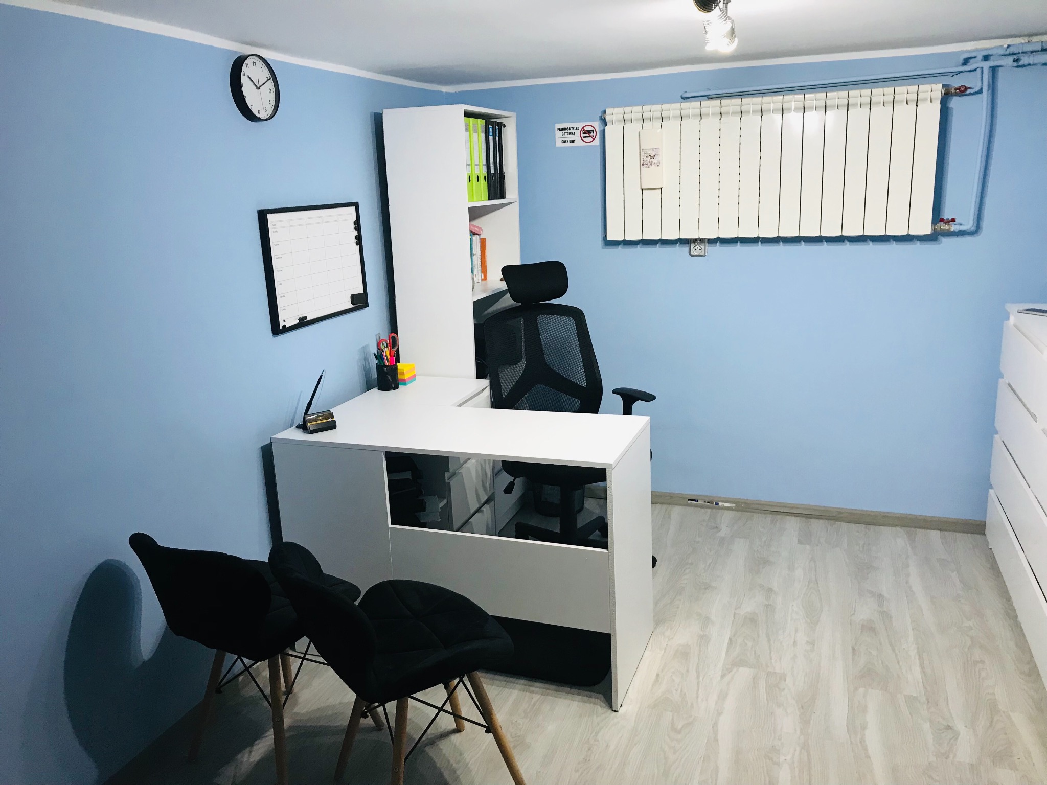 Jasne biuro dietetyka z biurkiem, krzesłami, regałem na dokumenty i tablicą suchościeralną na błękitnej ścianie.