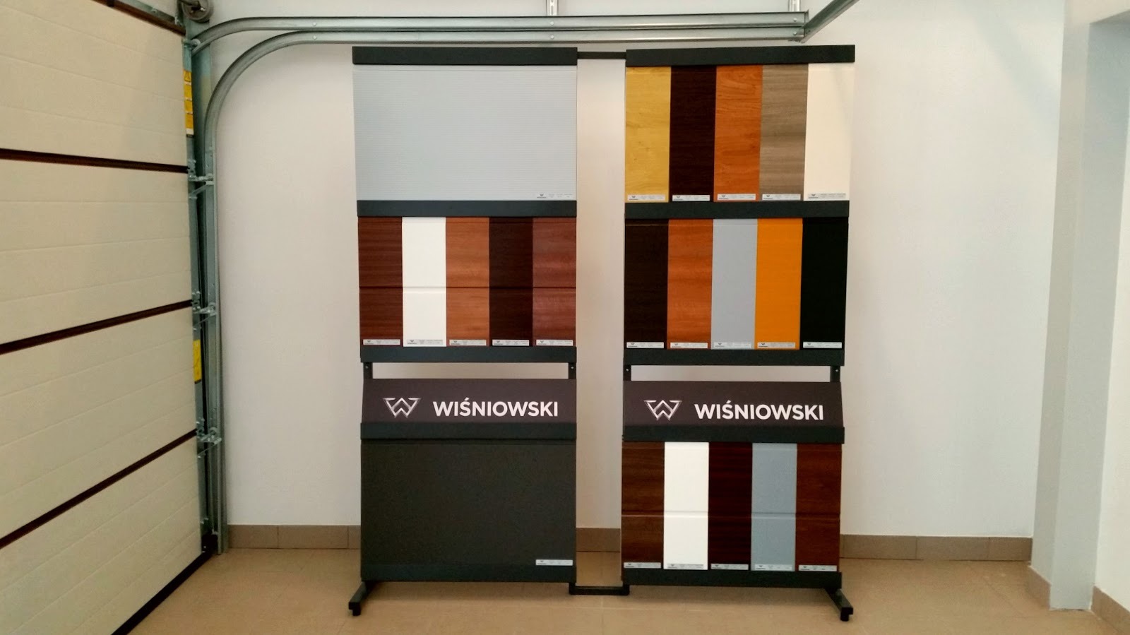 Ekspozycja próbek paneli bram garażowych marki Wiśniowski w salonie, widoczna brama segmentowa po lewej stronie.