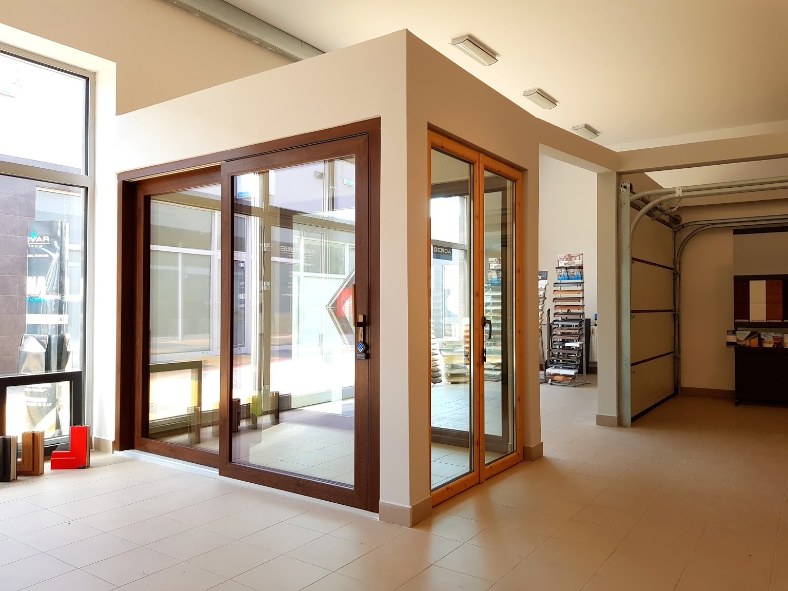 Ekspozycja w salonie: przesuwne okno z ciemnego drewna i drzwi balkonowe z jasnego drewna, widoczna brama garażowa w tle.