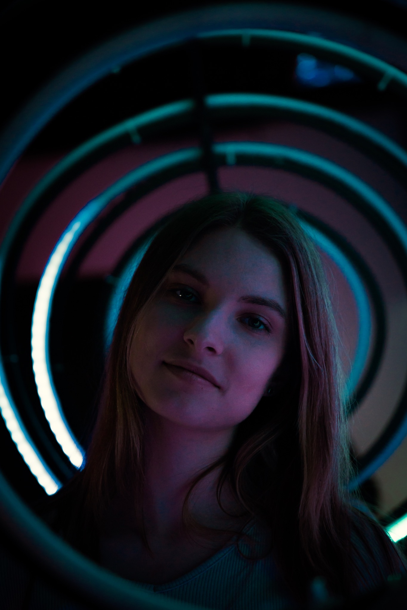 Portret kobiety z lekkim uśmiechem, oświetlonej niebiesko-fioletowym światłem neonowych okręgów w tle.