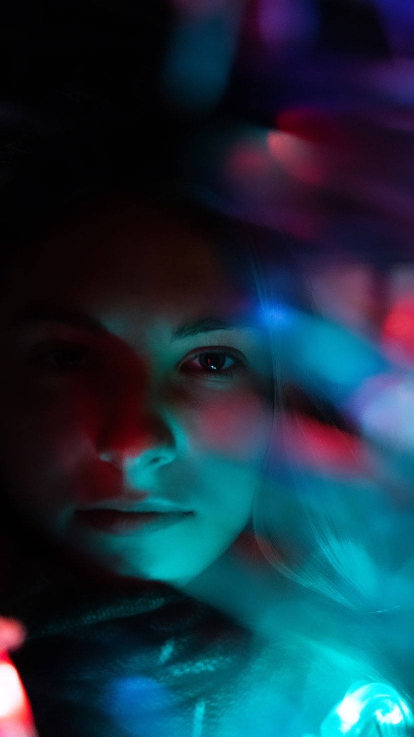 Portret młodej kobiety oświetlonej neonowymi światłami w odcieniach turkusu i czerwieni, tworząc artystyczny efekt rozmycia.