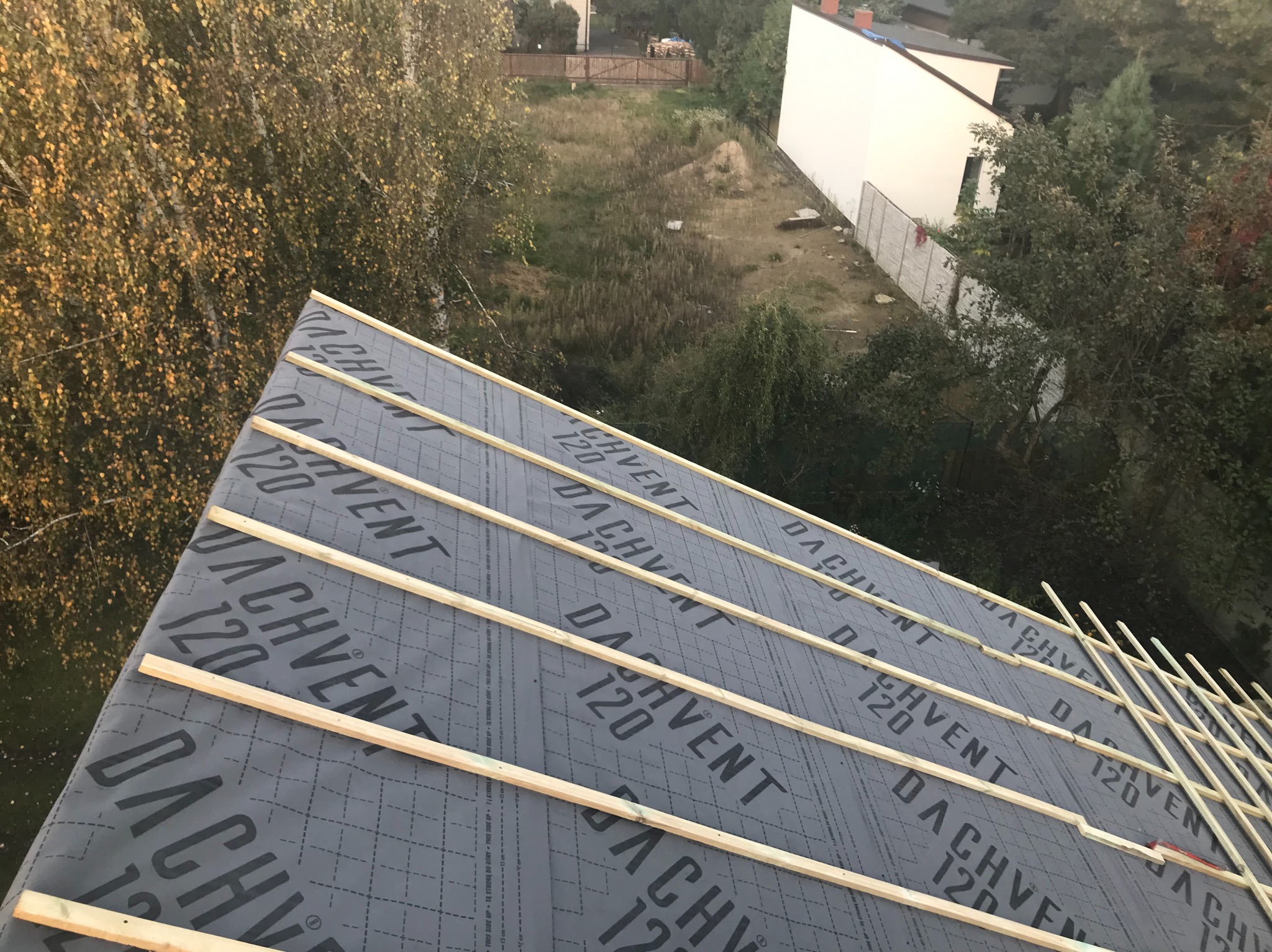 Widok z góry na konstrukcję dachu pokrytą membraną Dachvent 120 i drewnianymi łatami, przygotowaną pod dalsze etapy prac dekarskich, z zielonym otoczeniem w tle.