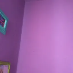 Fioletowa ściana w rogu pokoju z dwoma wiszącymi obrazami w ozdobnych ramkach.