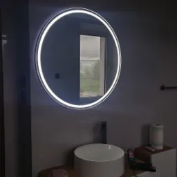 Nowoczesna łazienka: okrągłe lustro LED nad białą umywalką nablatową na szafce z drewnianym blatem. W tle widok z okna na zieleń.