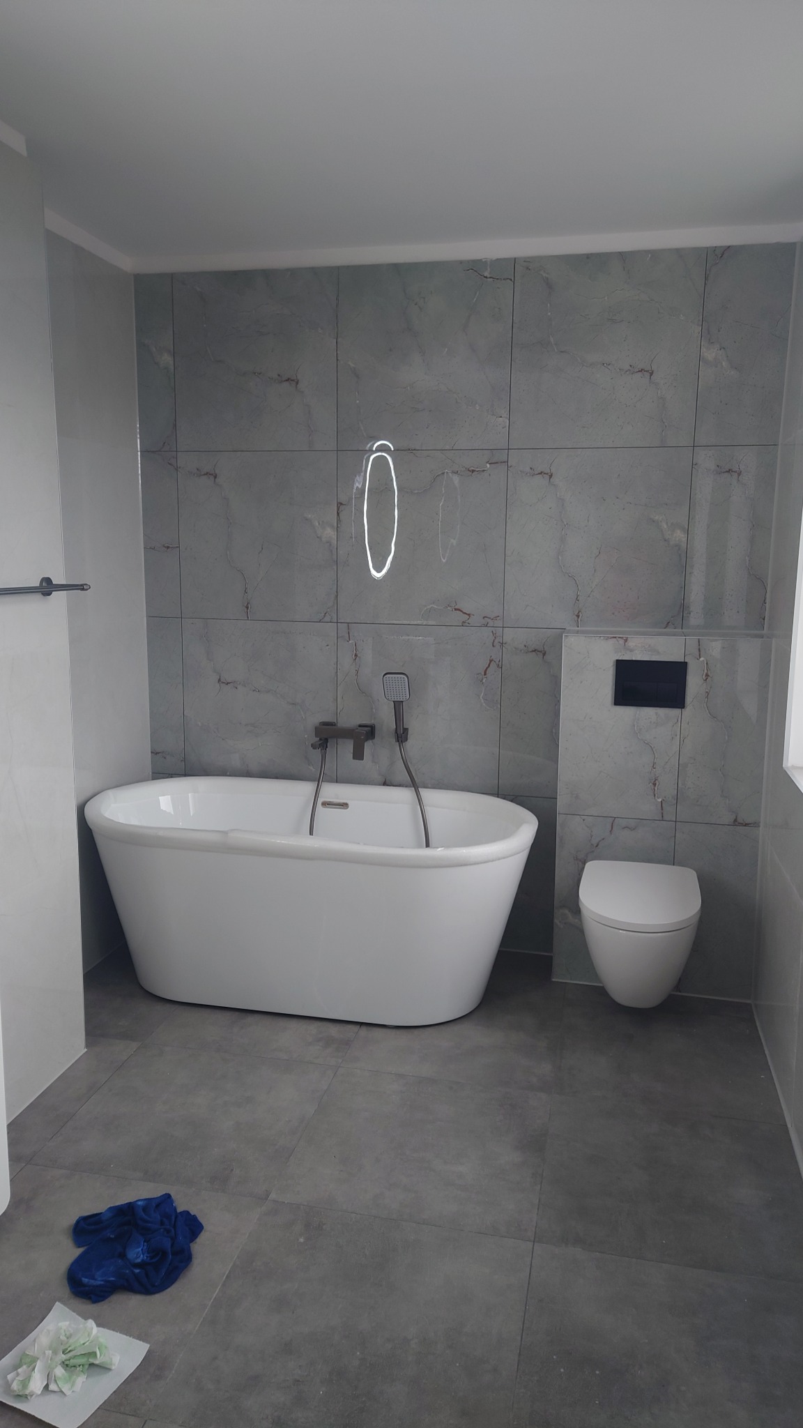 Nowoczesna łazienka z wolnostojącą wanną i szarymi płytkami imitującymi marmur. Widoczne elementy armatury w kolorze szczotkowanego brązu.