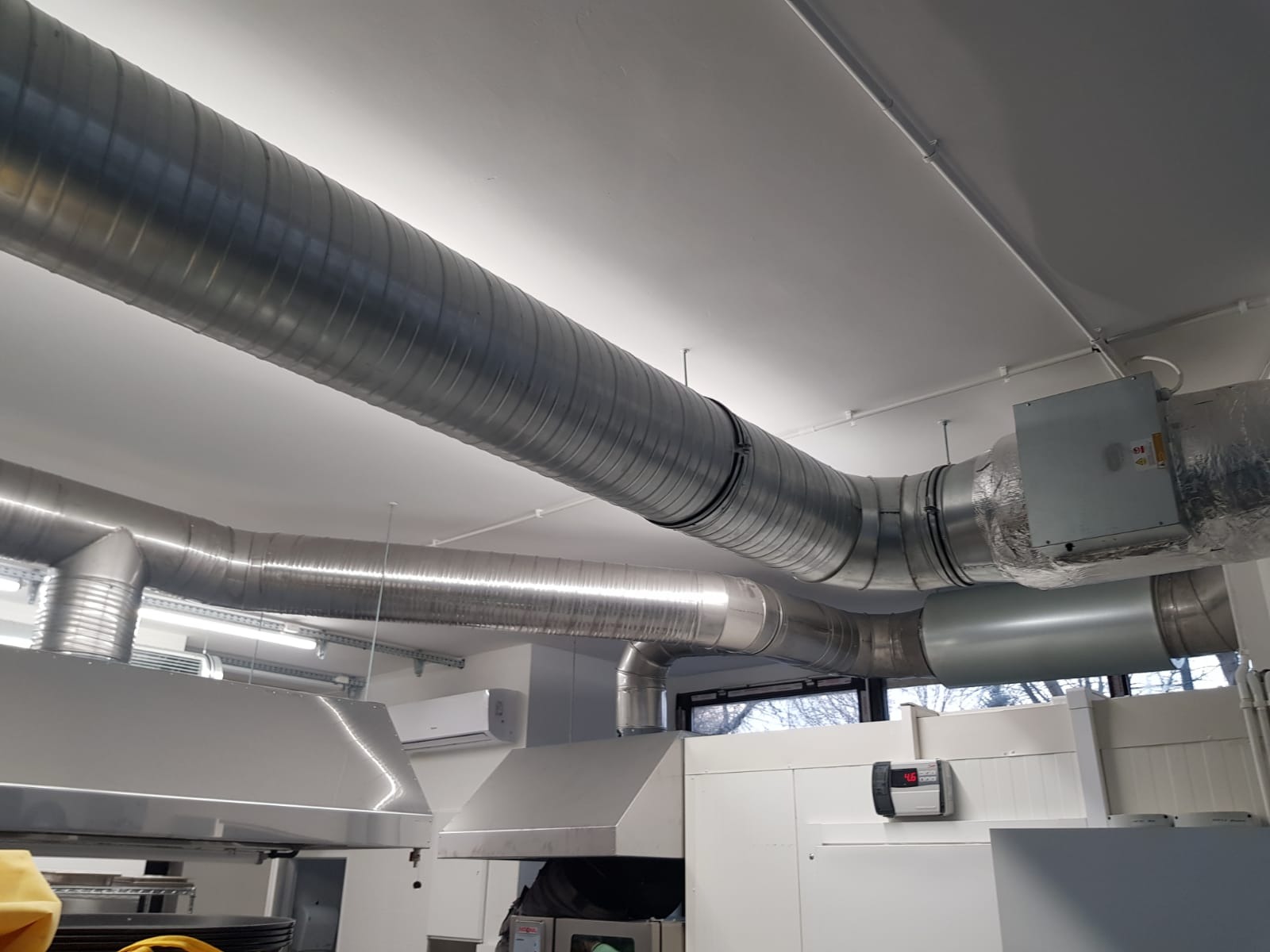 System kanałów wentylacyjnych z ocynkowanej blachy, zainstalowany pod sufitem w pomieszczeniu z elementami wyposażenia gastronomicznego, widoczny klimatyzator ścienny.