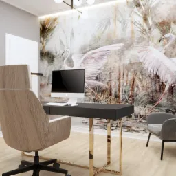 Nowoczesne biuro domowe z biurkiem na złotych nogach, komputerem i fototapetą z motywem ptaków, uzupełnione szarym fotelem i rośliną doniczkową.