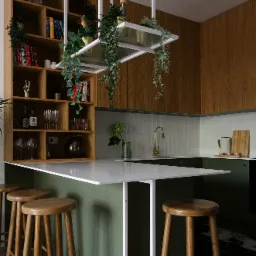 Stylowa kuchnia we Wrocławiu z zielonymi akcentami i drewnianymi elementami, wyspa z białym blatem i hokerami, wisząca konstrukcja z roślinami, półki z książkami i dekoracjami.