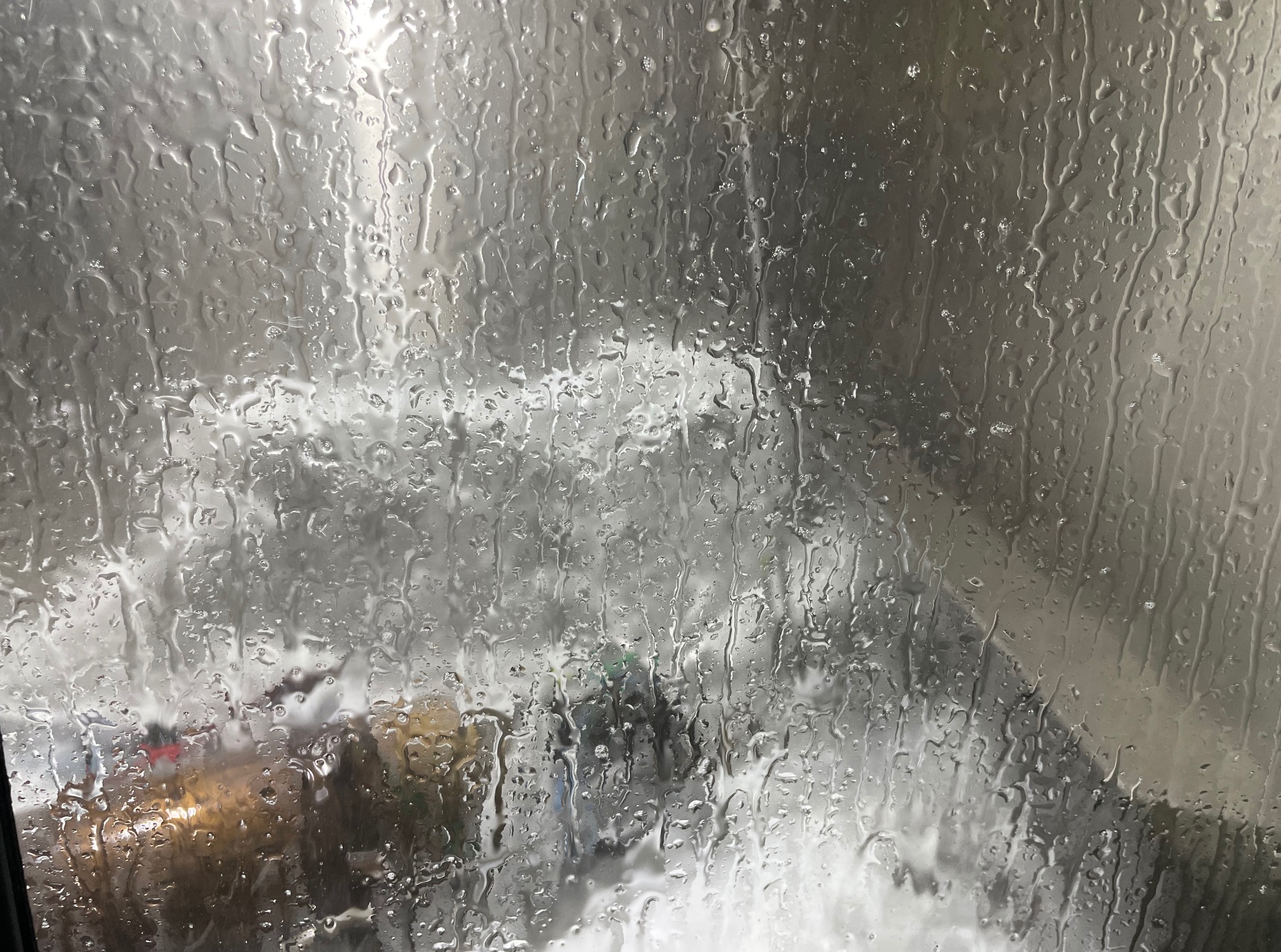 Deszcz na szybie samochodu w Wolicy. Krople wody zniekształcają widok na zewnątrz, tworząc abstrakcyjny obraz ulicy i świateł.