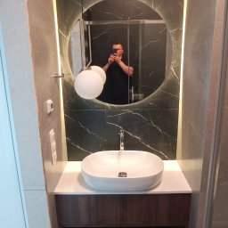 Pro_Poziom - Nowoczesna łazienka z umywalką nablatową, podświetlanym okrągłym lustrem i ciemnymi płytkami imitującymi marmur, widoczne odbicie fotografa w lustrze.